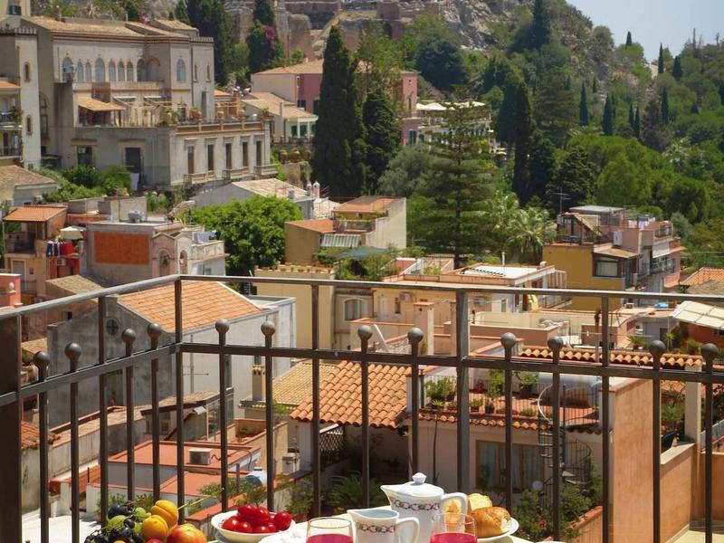 Breakfast table with fruit and juice on balcony overlooking town and hills.