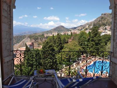 Balkon mit Tisch, Stühlen und Blick auf Pool und Berge unter blauem Himmel.