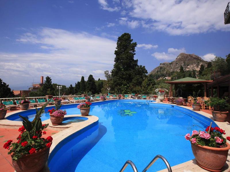 Large pool with blue water, surrounded by terracotta tiles and potted plants.