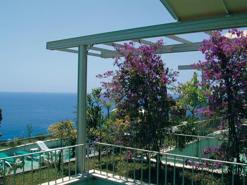 Overdekt terras met bloeiende planten en uitzicht op zee op een zonnige dag.