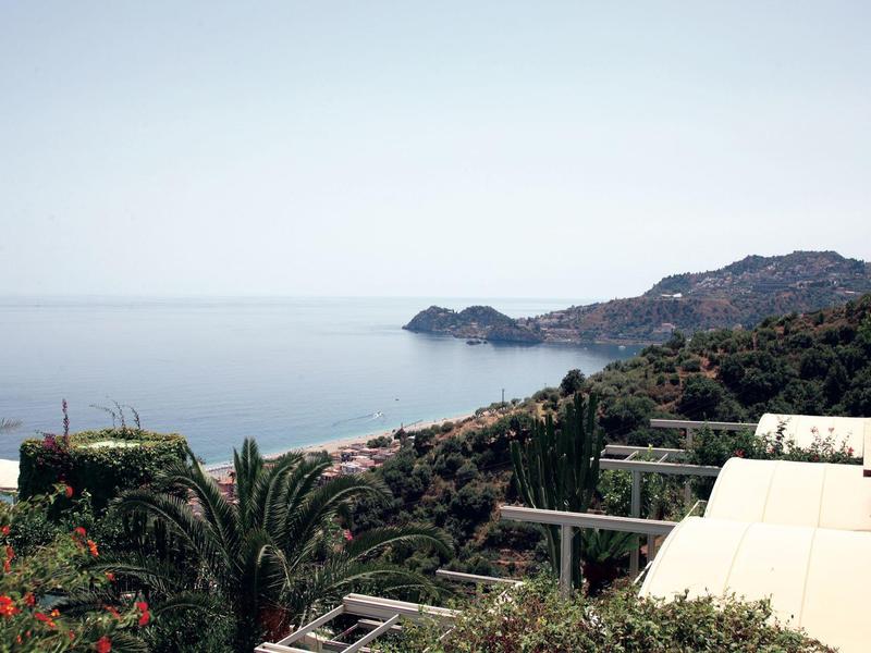 Uitzicht op een kustlandschap met palmbomen, villa's en kalme zee onder een heldere lucht.