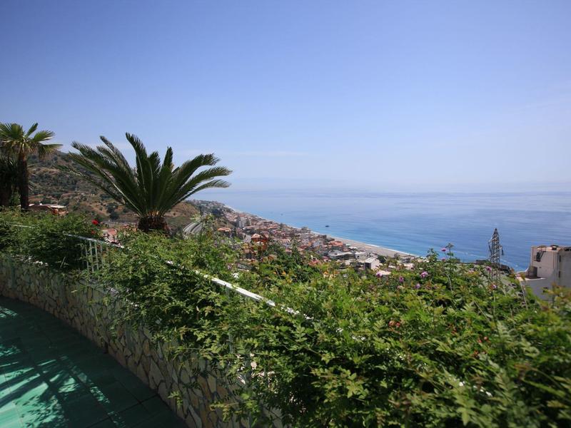 Uitzicht op een kustplaats met palmbomen en een zwembad op de voorgrond onder een heldere lucht.