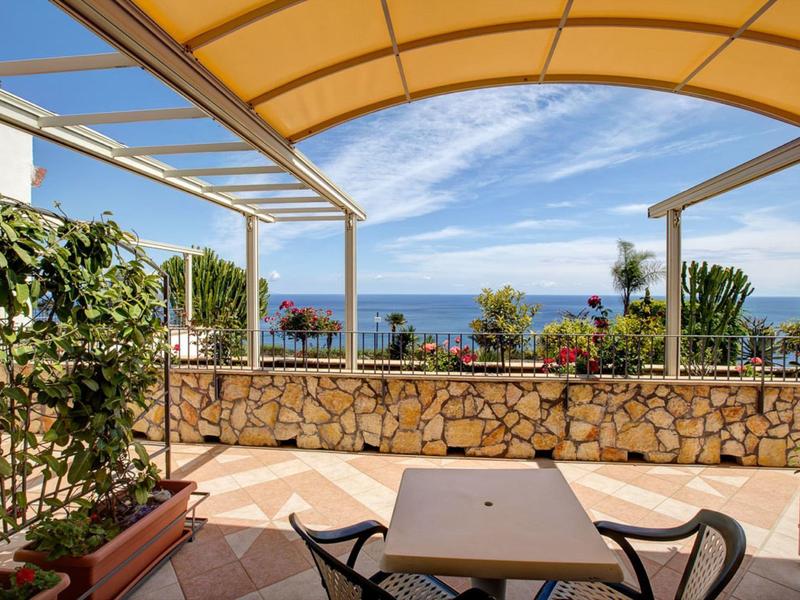 Terras met pergola, uitzicht op zee en bloeiende planten op de voorgrond.