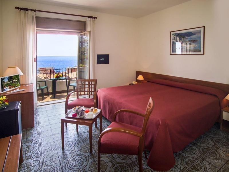 Helles Hotelzimmer mit Doppelbett, Balkon mit Meerblick und traditionellen Fliesenboden.