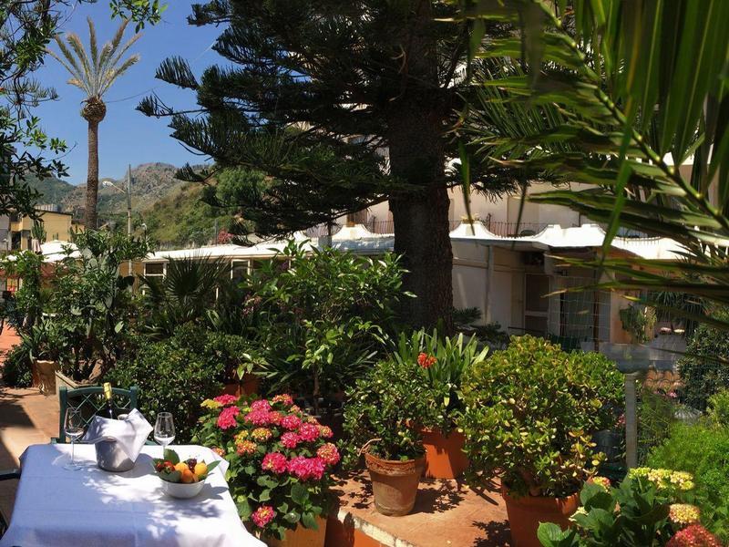 Gemütliche Terrasse mit weiß gedecktem Tisch, Blumen, Bäumen und Sonnenschirmen im Garten.