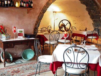 Gemütliches Restaurant mit bordeauxroten Tischtüchern, schmiedeeisernen Stühlen und rustikalen Steinbögen.