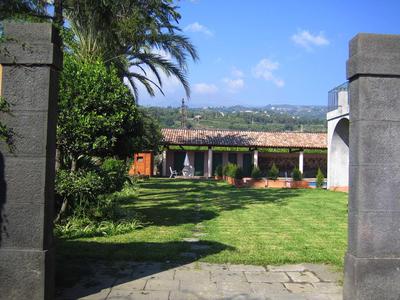 Blick durch einen steinernen Torbogen auf einen Garten mit Rasen und einem Gebäude mit Säulengang.