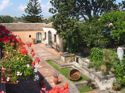 Innenhof mit Blumentöpfen, Steinbrunnen und mediterranen Gebäuden unter blauem Himmel.