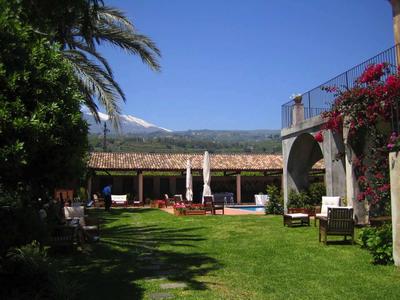 Sonniger Hotelgarten mit Stühlen, Tischen und blühenden Pflanzen unter blauem Himmel.