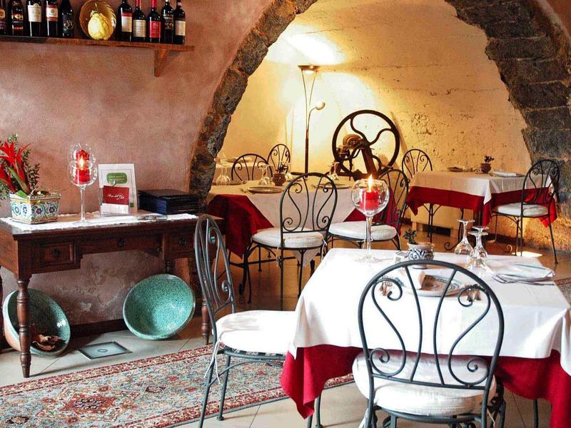 Gemütliches Restaurant mit bordeauxroten Tischtüchern, schmiedeeisernen Stühlen und rustikalen Steinbögen.