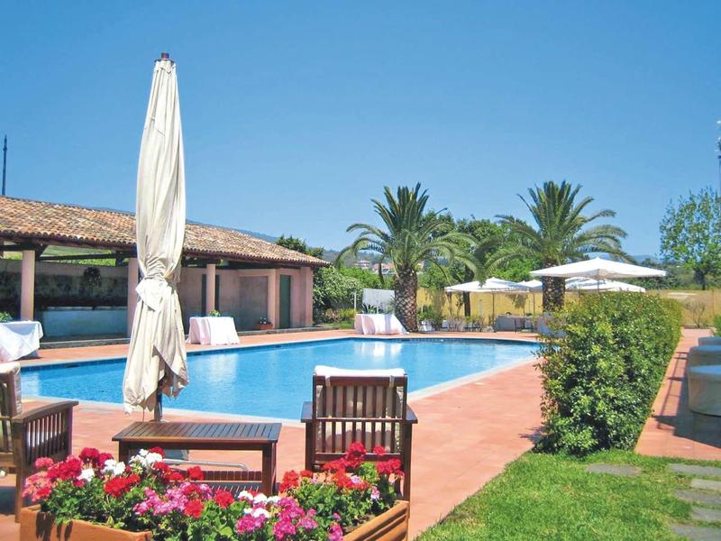 Großer rechteckiger Pool mit blauer Wasserfläche, von Stühlen, Sonnenschirmen und Palmen umgeben.