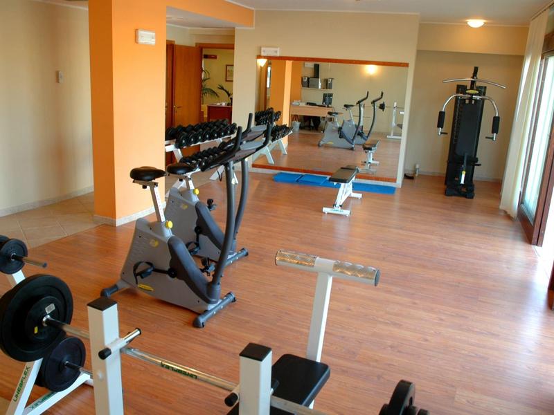 Malá posilovna s rotopedem, posilovací lavicí a zrcadlovou stěnou.