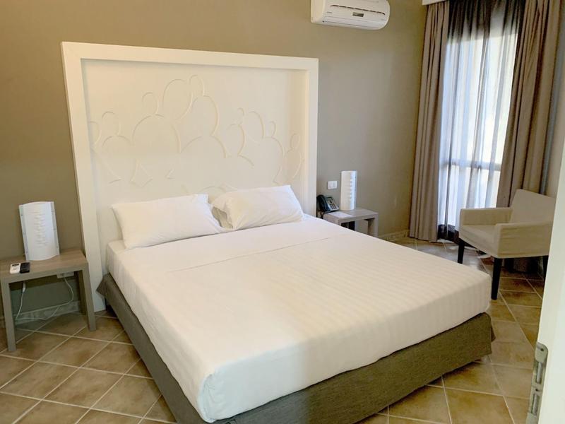 Ložnice s velkou postelí, nočními stolky a křeslem vedle okna se závěsy.