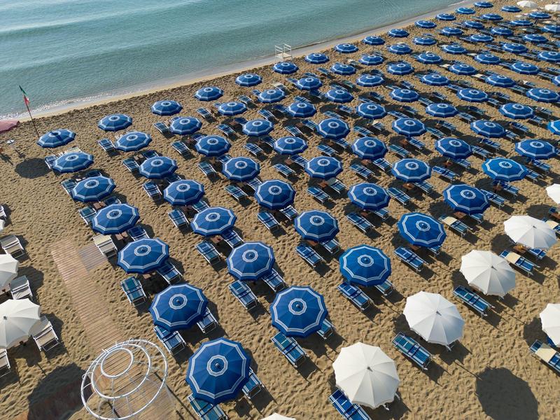 Pláž s rovnoměrně uspořádanými modrými a bílými slunečníky podél pobřeží.