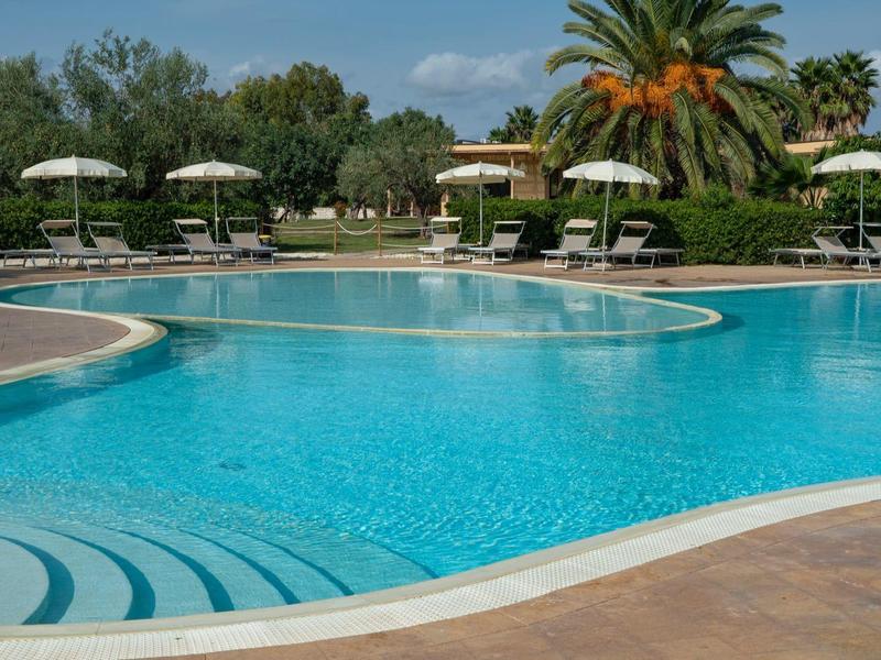 Velký průzračný bazén s lehátky a slunečníky v slunném hotelovém resortu.