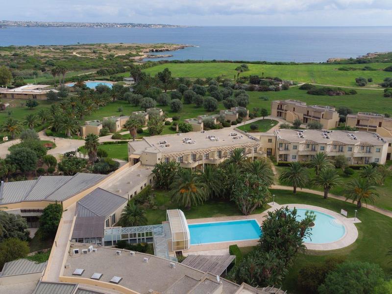 Letecký pohled na hotel s bazénem, zahradami a mořem v pozadí.