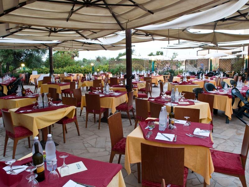 Restauranční terasa s prostřenými stoly a barevnými ubrusy pod sluneční ochranou.