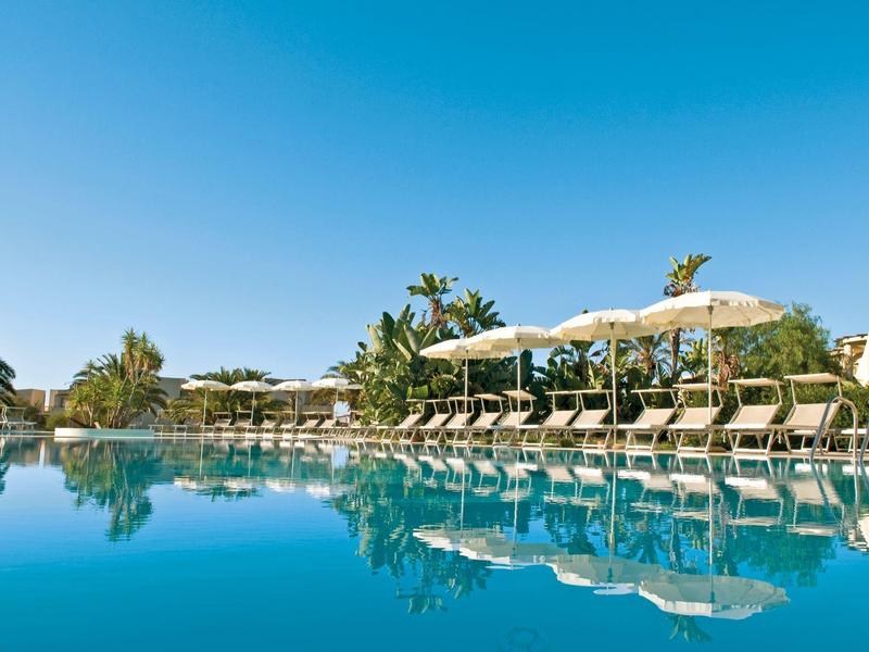 Velký hotelový bazén s lehátky a slunečníky pod jasně modrou oblohou.