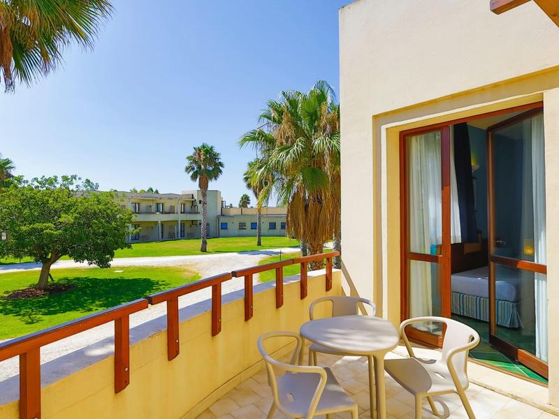 Balkon s stolem a židlemi s výhledem na zahradu a palmy na slunci.