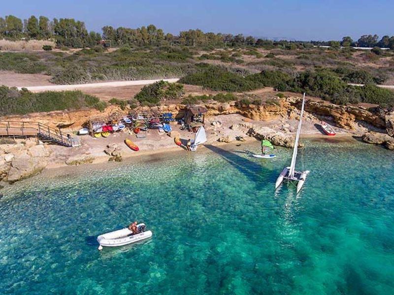 Čirá tyrkysová voda s loděmi a skalnatým pobřežím pod modrou oblohou.