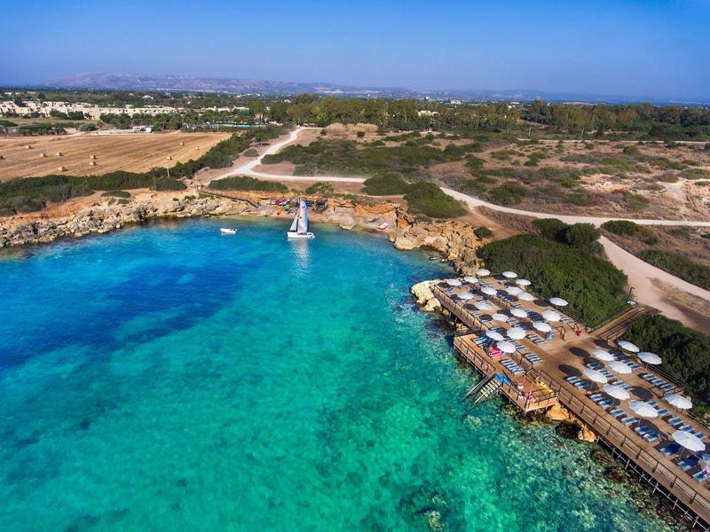 Čistá tyrkysová voda u pobřeží s plachetnicí a lehátky na dřevěných molách.