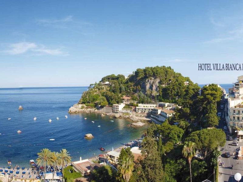 Panorama einer Küstenstadt mit blauem Meer, Sandstrand, Booten und grünen Hügeln im Hintergrund.