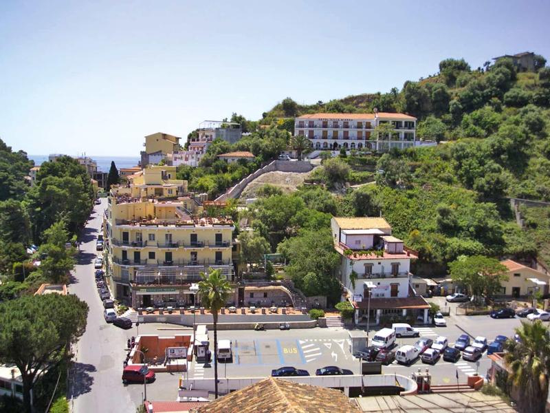 Küstenstadt mit Parkplätzen, mehrstöckigen Gebäuden und bewaldeten Hügeln unter klarem Himmel.