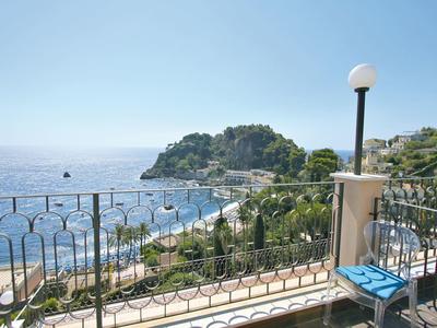 Balcone con sedia e lampada con vista su una città costiera e il mare sullo sfondo.