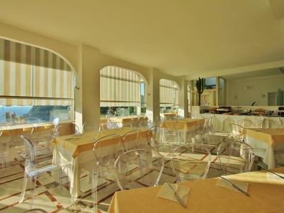 Ristorante luminoso con tavoli apparecchiati e sedie trasparenti con vista sul mare.