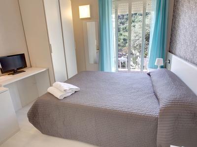 Camera d'albergo moderna con letto matrimoniale, TV, armadio e balcone con tenda blu.