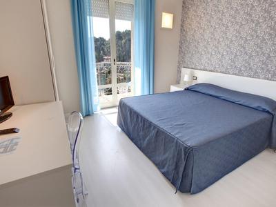 Piccola camera d'albergo con letto matrimoniale, scrivania, TV e balcone con vista.