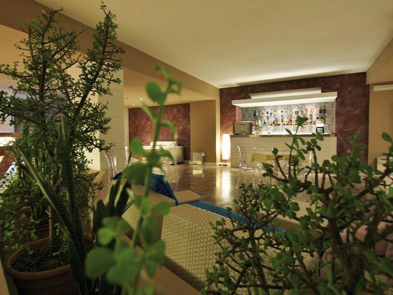 Reception dell'hotel con bancone, arredi moderni e piante verdi in primo piano.