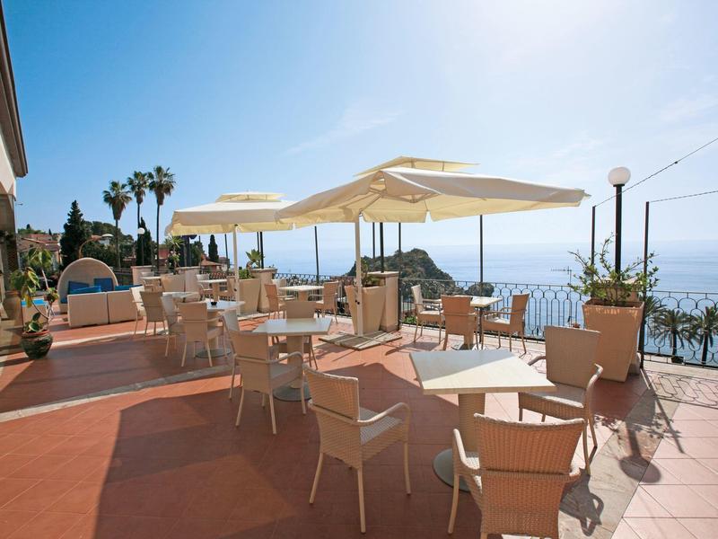 Terrazza con tavoli, sedie e ombrelloni con vista mare sotto un cielo limpido.