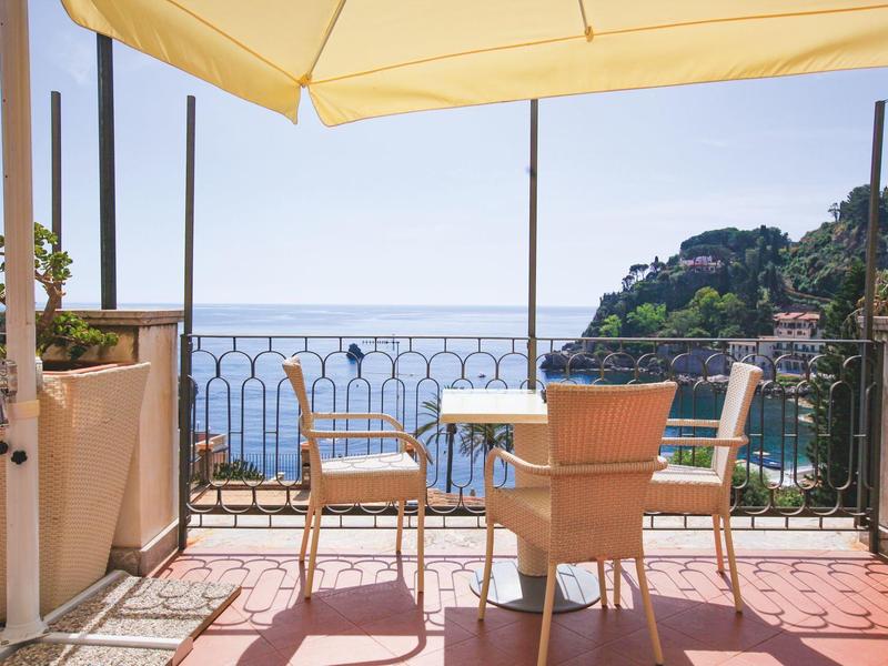Terrazza con sedie e tavolo sotto ombrellone con vista sul mare e sulle colline.