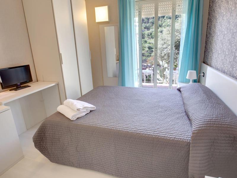 Camera d'albergo moderna con letto matrimoniale, TV, armadio e balcone con tenda blu.