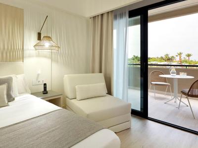 Modernes Hotelzimmer mit Bett, Sitzecke und Balkon mit Blick auf die Terrasse.