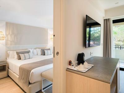 Modern eingerichtetes Hotelzimmer mit Doppelbett, Fernsehgerät und Balkon mit Blick ins Grüne.