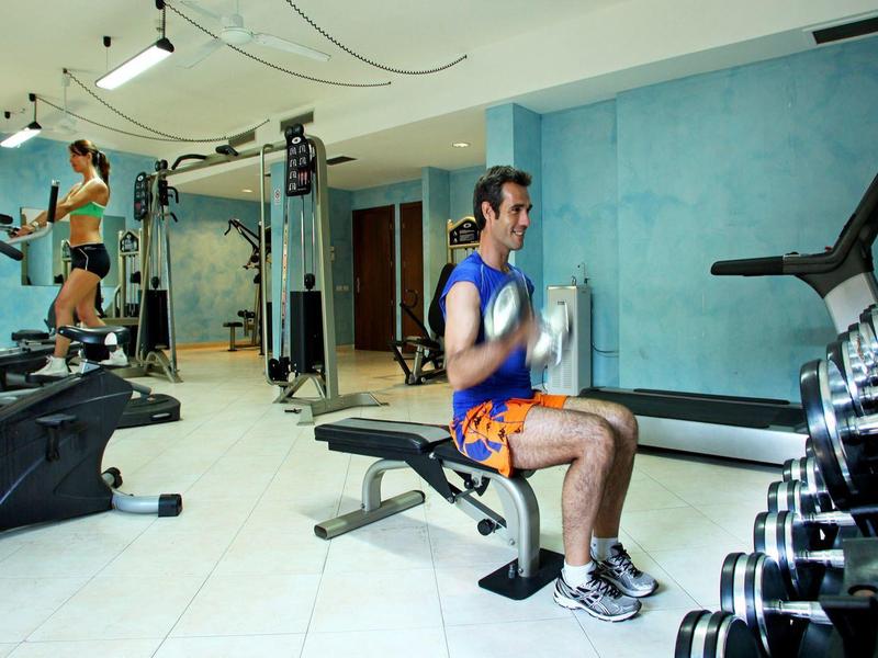 Two men exercising in a gym with workout bikes and dumbbells in a modern indoor setting.