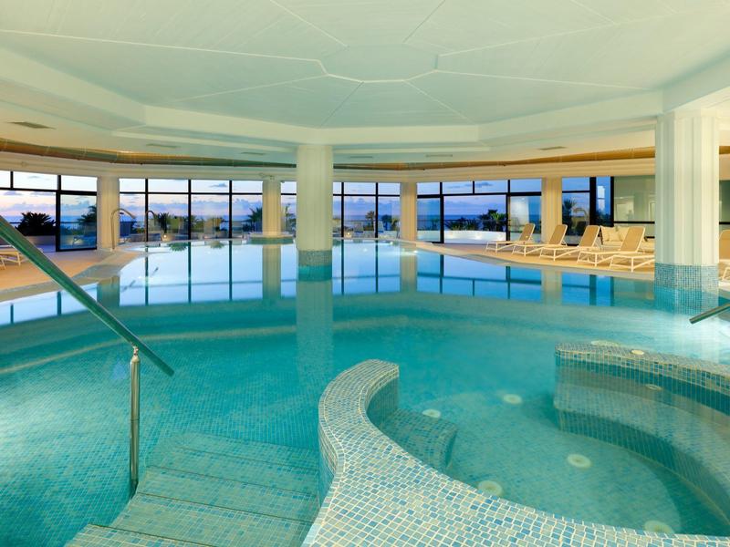 Indoor pool area with a hot tub, lounge chairs, and large windows overlooking the outdoors.
