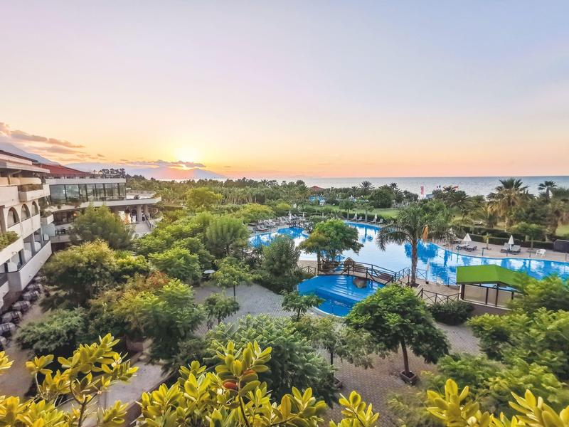 Hotel with lush gardens, multiple pools, and ocean view at sunset.