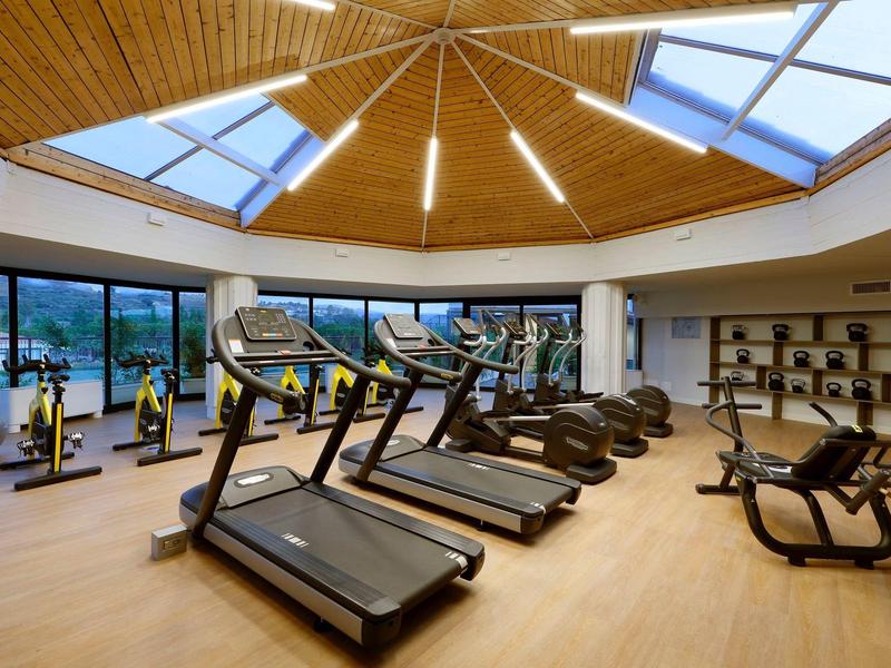 Modern gym with treadmills, exercise bikes, and elliptical trainers under a wooden ceiling with skylights.