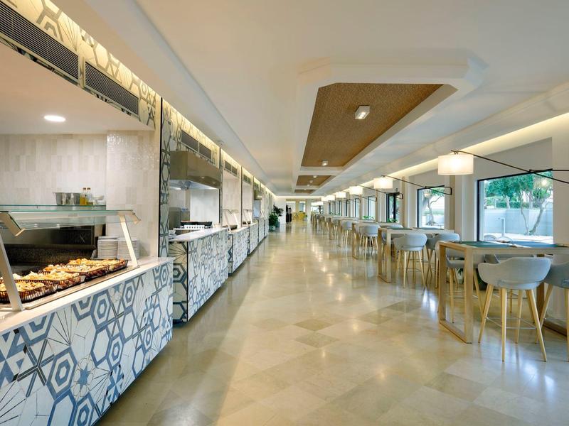 Long, bright hotel dining area with buffet counter on left and tables on right.