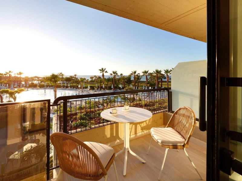 Balcony with two chairs and a round table overlooking a waterfront at sunset.