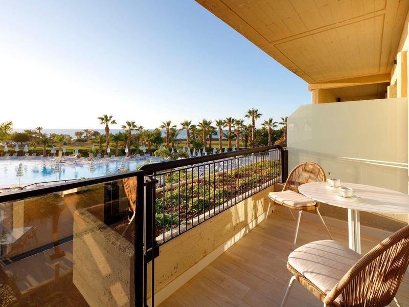 Balcony with chairs overlooking a pool and palm trees under a clear sky.