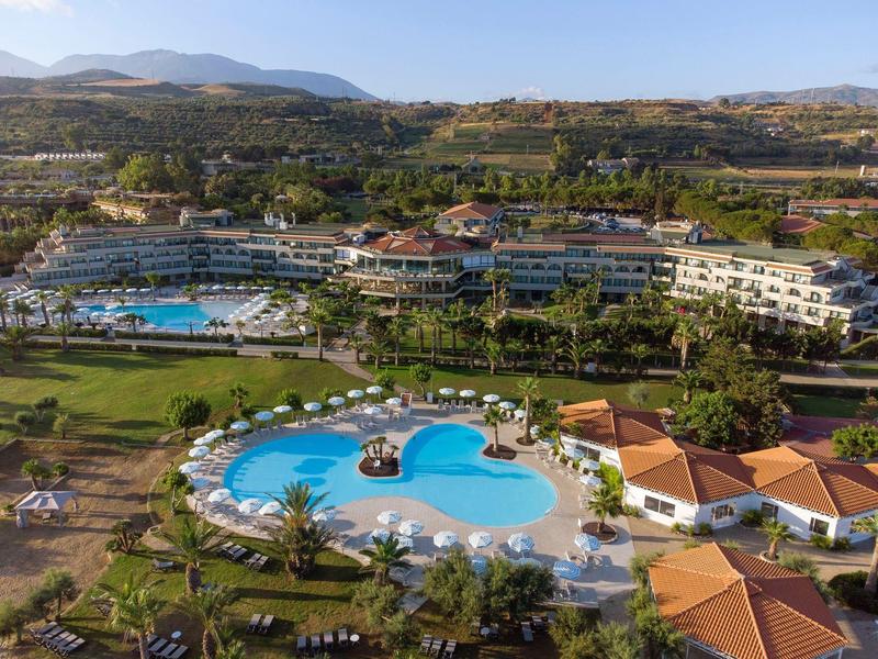 Resort with multiple pools, surrounded by greenery and hills in the background.