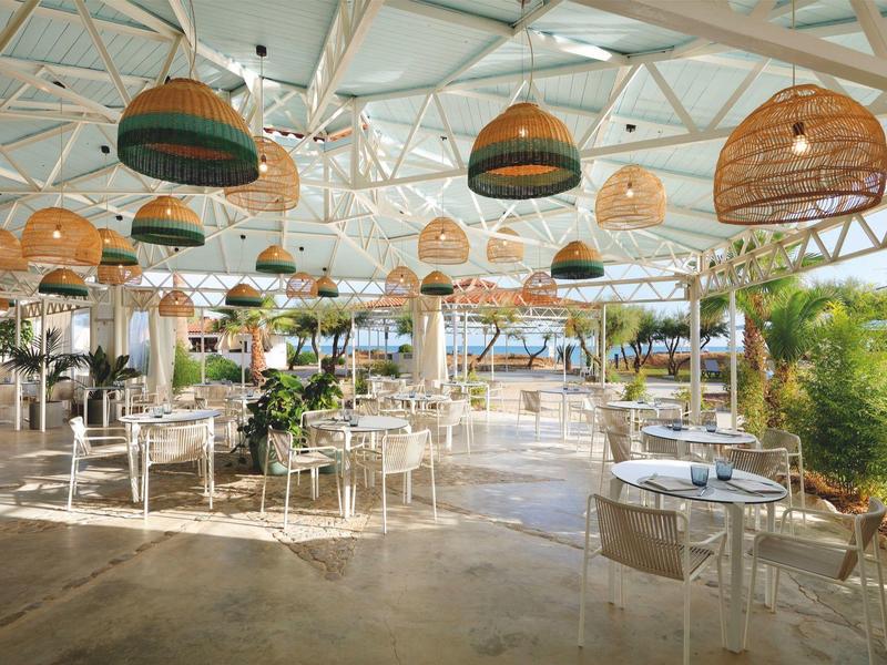 Spacious modern outdoor dining area with white chairs, tables, and hanging wicker lamps under a glass roof.