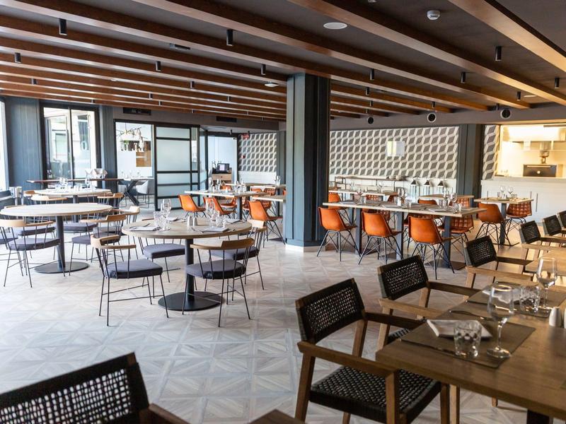 Modern hotel dining area with wooden beams, mixed seating, and large windows providing natural light.