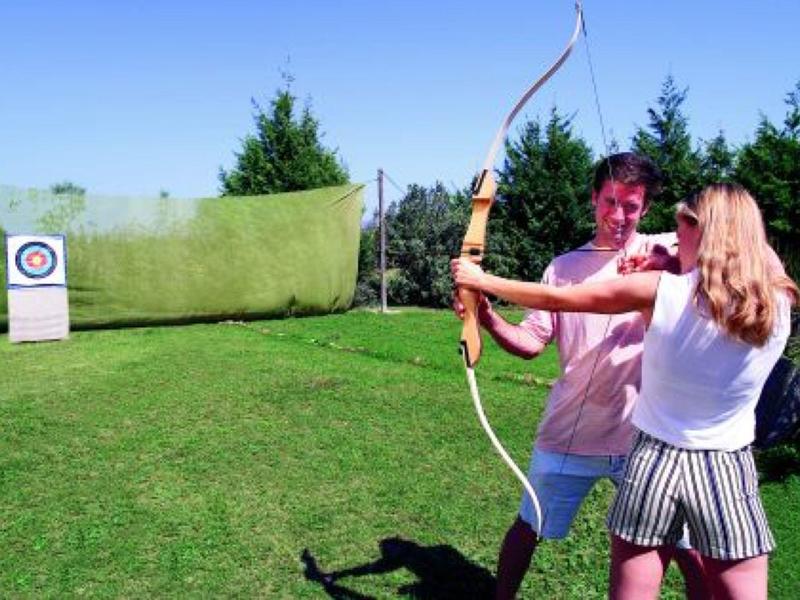 Two people practicing archery outdoors on a grassy field with trees in the background.