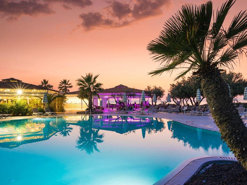 Calm resort pool at sunset with palm trees and lit buildings.