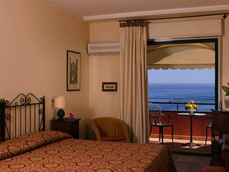 Comfortabele hotelkamer met tweepersoonsbed en balkon met uitzicht op zee.